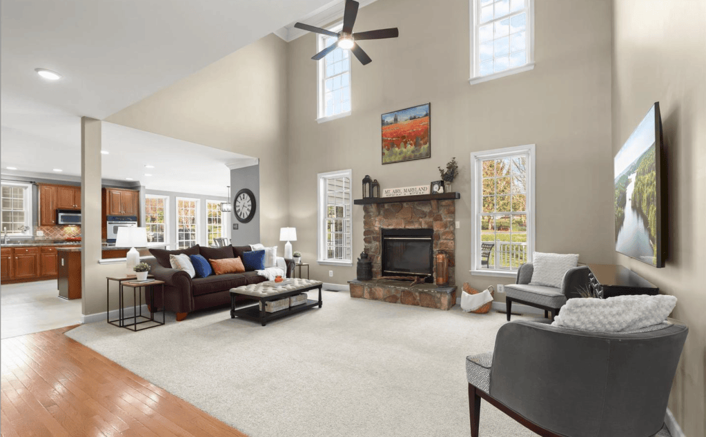 Bright and spacious living room featuring a stone fireplace, large windows, and a cozy seating arrangement with decorative cushions.