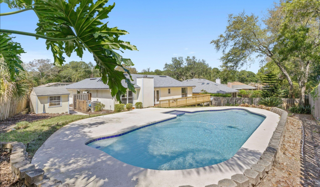 Backyard with a swimming pool, surrounded by greenery and a wooden deck in a residential area.